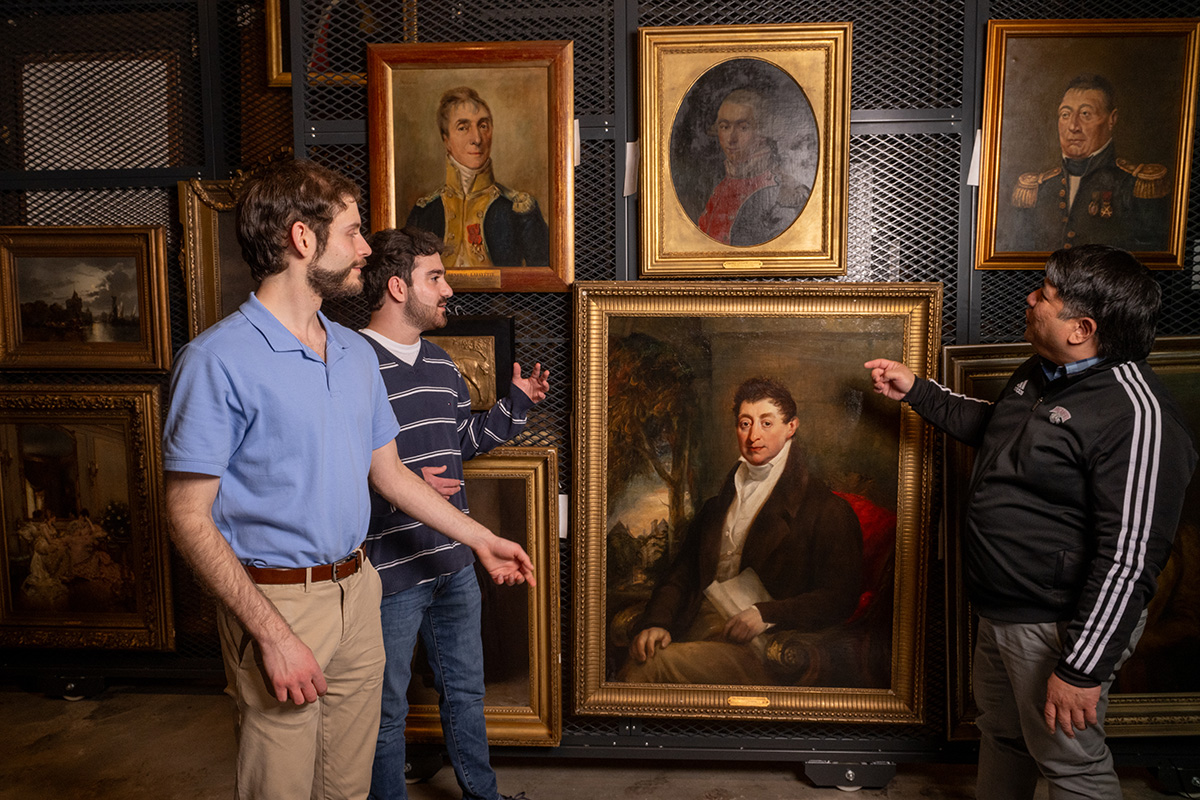 Christopher Byrnes ’26, Peter Godziela ’25, and Rico Reyes point to art in the gallery.