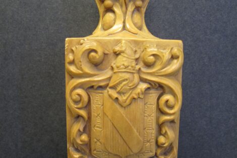 The photo of the Lafayette College mace shows the College seal and coat of arms of the Marquis de Lafayette. A detailed shot of the top of the mace is shown on a gray background.