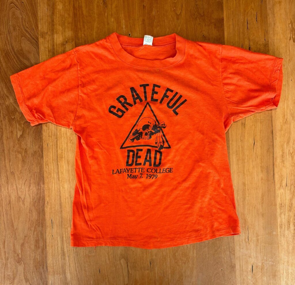 An overhead view of an orange Grateful Dead t-shirt placed on a wooden table