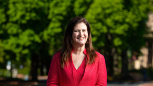 Nicole Hurd smiles on campus with a green tree behind